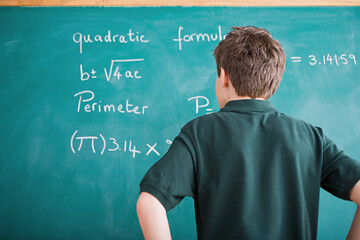 Boy standing in front of blackboard looking at mathematical formula