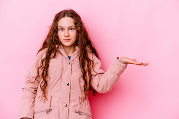 Little caucasian girl isolated on pink background showing a copy space on a palm and holding another hand on waist.