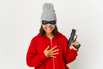 Young robber hispanic woman wearing a mask laughs out loudly keeping hand on chest.