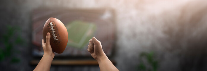 Excited man watching an American football game in front of his television with his ball in hand