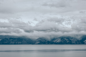 Fototapeta na wymiar Dramatic clouds over the lake and in the mountains. Gray foggy morning, cloudy weather. Lake Baikal, Russia.