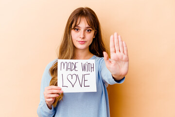 Young caucasian woman holding a made with love placard isolated standing with outstretched hand showing stop sign, preventing you.