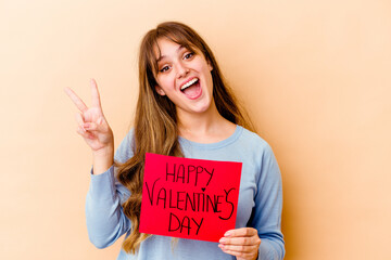 Fototapeta na wymiar Young caucasian woman holding a Happy Valentines day isolated joyful and carefree showing a peace symbol with fingers.