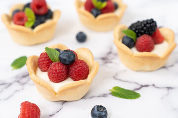 Delicious pastry mini fruit cream cheese pies or tart cakes with fresh raspberry, blueberry and blackberry