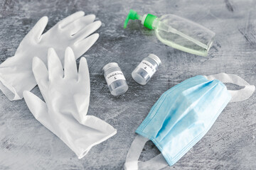 covid-19 vaccine race and immunisation against the pandemic, ampoules with Vaccine 1 and Vaccine 2 labels side by side next to disposable gloves, hand sanitizer and face mask