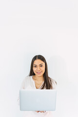 Pretty young woman looks sitting on the floor with laptop looking at the camera with white background