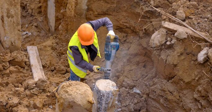 A builder cleaves a piece of a concrete pile with a powerful industrial perforator