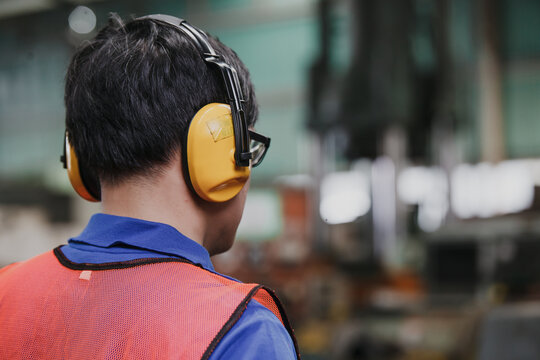 Portrait of young Asian engineer worker wearing protective headphones posing
