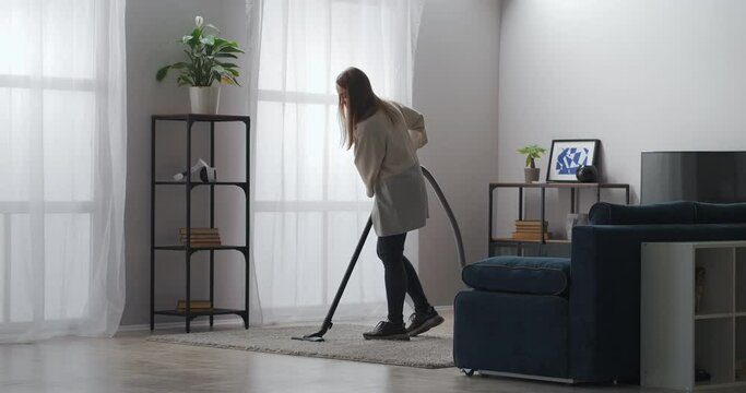 cleaning service, female worker is cleaning carpet in living room of modern apartment, using vacuum cleaner