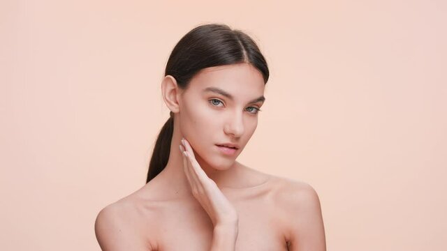 Medium close-up beauty portrait of Young slim woman who gently touches and strokes her jawline and look at the camera | Beauty and skin care concept