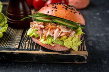 Close up of fish burger with pink bun and salmon on black. Omega 3 fats healthy for brain. Home...
