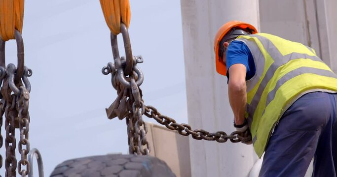 On a construction site, a worker hooks crane hooks to a massive load and carries it to the right place. 