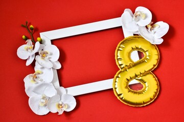 Greeting Card International Women's Day on March 8th. White frame with orchid flowers and number 8 on a red background. minimalism. Greeting card. View from above. Place for text.