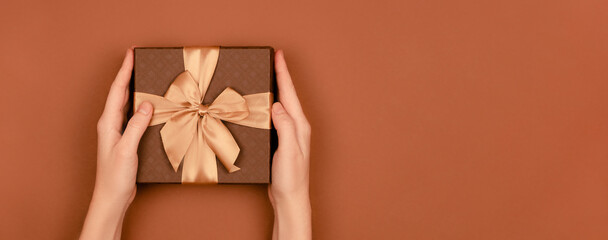 Female hands holding a festive box with ribbons and bows. Red festive background top horizontal...