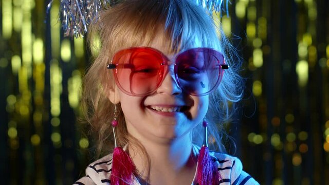 Portrait of trendy stylish girl looking at camera, smiling. Elegant child kid in neon lighting posing at disco party cyberpunk club. Futuristic hipster teenager children making faces, fooling around