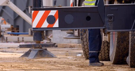 At a construction site, a multi-axle powerful mobile crane is preparing to lift a load, operator extends outriggers for work