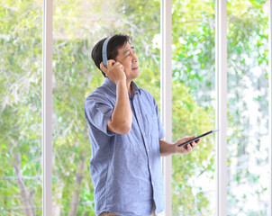 A senior man listening to music via headphones with wireless tablet computer in hand with happiness manner. Idea for a lifestyle of older people with modern communication technology.