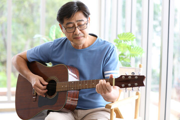 A senior man sitting and playing guitar with easy relax concentration manner
