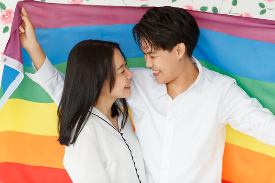 LGBTQ Couple Lovers, A Handsome Girl As A Man Or Butch Femme Covered .with The Rainbow Flag The Symbol Of LGBT, Spending And Sharing Loving Time With Fun, Warmth, And Happiness