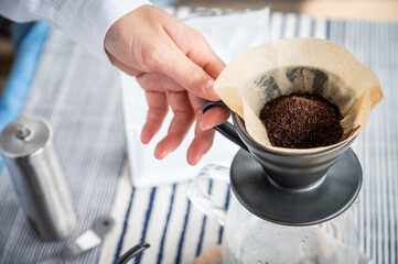 Barista hand holding a dripper with ground coffee inside with paper filter before making fresh brewed coffee.