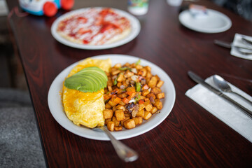 Omelette, roasted potatoes and avocado slices on a white plate