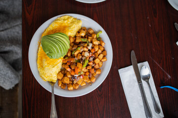 Omelette, roasted potatoes and avocado slices on a white plate
