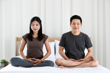 Fototapeta na wymiar Man and woman Buddhist sitting on bed in the bedroom and doing meditation in Buddhism religion style together. The idea for faith and trust in religion and calm of mind