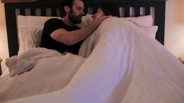 Happy young couple in bed together on their cell phones lying awake. HD 24FPS.