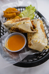 Spicy pork burritos and lettuce in a plastic basket
