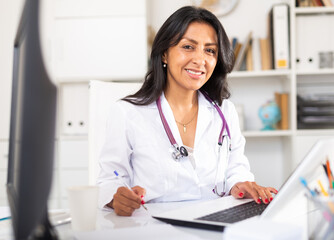 Portrait of smiling Colombian woman physician consulting patient in medical office