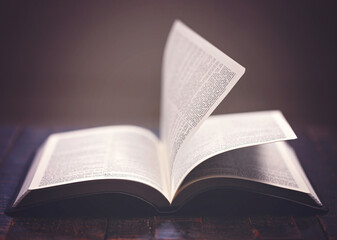 A Bible Open on a Rustic Wooden Table with Pages Blowing Open