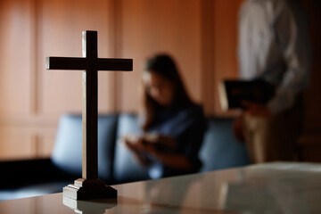 Close up cross is blur background. Asian Christian woman and man holding hands in praying for...