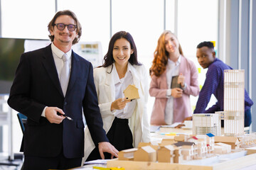 A man caucasian manager and young businesswoman picks up a house model to take pictures to promote real estate in the office. Concept business promote.