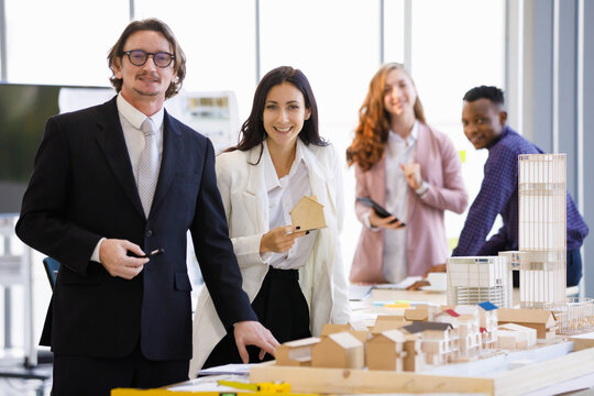 A man caucasian manager and young businesswoman picks up a house model to take pictures to promote real estate in the office. Concept business promote.