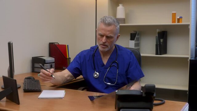 Concerned male doctor examines chest x-ray of sick patient holding it up to the light for a better view and takes notes