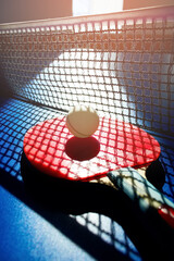 A red table tennis racket and a white ball lie on the surface of the table next to the net. Sports game and active recreation.