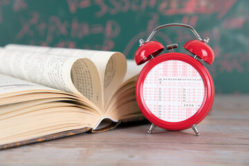 In front of the blackboard, a book is folded into love and an alarm clock with an answer card