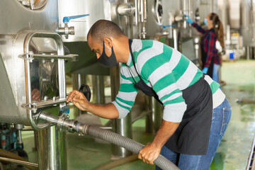 Portrait of male winery worker in mask working with metal tanks for wine fermentation