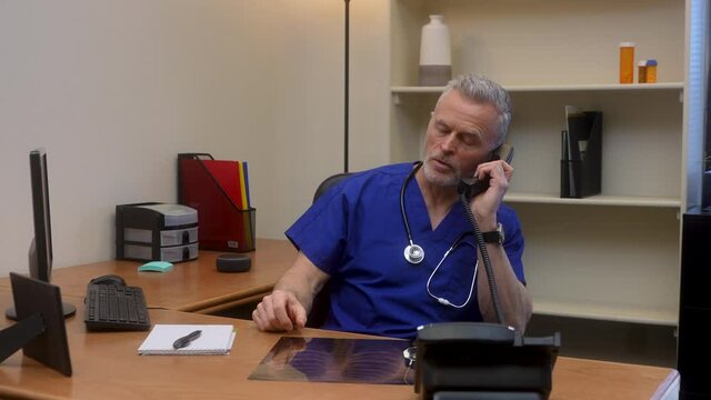 Male doctor examines chest x-ray then makes a phone call to colleague to discuss diagnoses