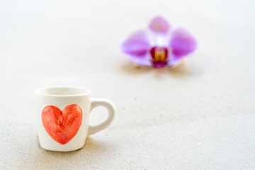 Obraz na płótnie Canvas cup coffee with red heart printed and blossom phaleanopsis orchid on sandy background. 