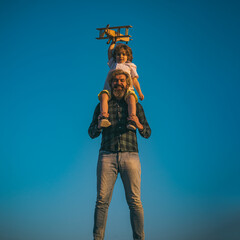 Fototapeta na wymiar Father and son playing with wooden airplane. Boy sitting on fathers shoulders.