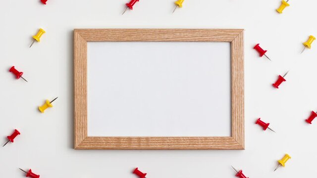 Yellow red push pins and wooden frame on white background. Stop motion animation flat lay top view. Education back to school and online study concept with copy space