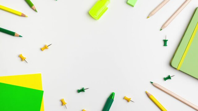 Green and yellow pen, sticky note, notepad, marker, eraser, push pins, paper clip pencils on white background Stop motion animation flat lay top view. Education back to school and online study concept