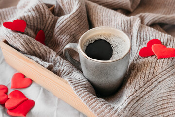 ceramic grey cup with black coffee in cozy atmosphere on beige crumpled fabric of bed and lots of red hearts decor. Surprise for loved , gift idea for Valentine's Day