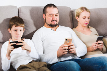 Modern young family sitting with smartphones in home interior