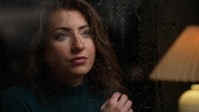 Close up of woman looking out at  her neighborhood ona rainy night as lightning flashes. Cinematic