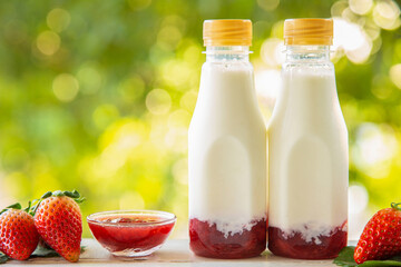 Homemade strawberry milk in a bottle on white wooden table with strawberry fruits with nature background