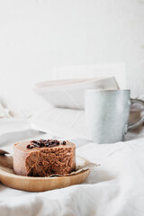 small round chocolate cheesecake without baking on reusable bamboo plate on cozy beige blanket with cup coffee and book. maintaining mental health, time spent in pleasure. vertical, selective focus