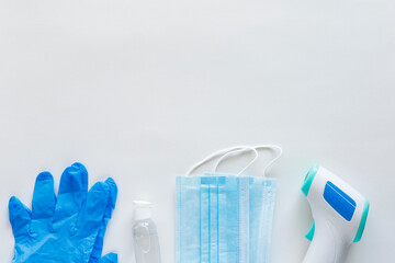 Corona virus protection concept flat lay. Non-contact infrared body thermometer, latex gloves, disposable masks and sanitizer on white background with copy space.