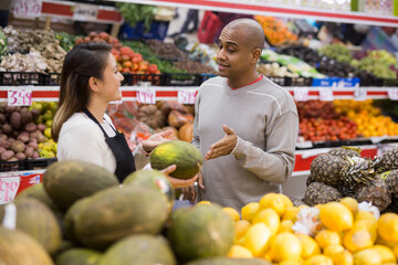 Latin man in fruit section of supermarket with shop worker helping him